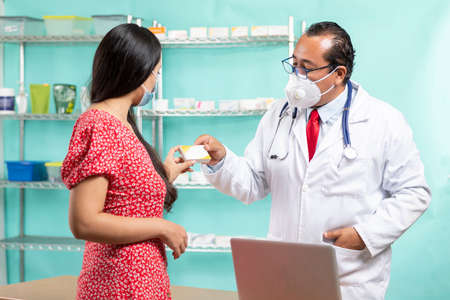 Proud enterprising man in his pharmacy, showing the medicines and attending a pacient. Interior...
