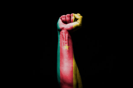 Strong man's hand in battle signal with Cameroon flag on black background.の写真素材