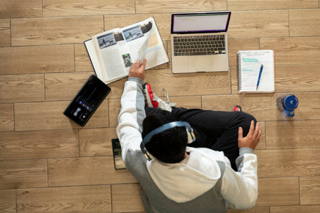 Young man with headphones sitting on the floor of his house studying and working at home with a...
