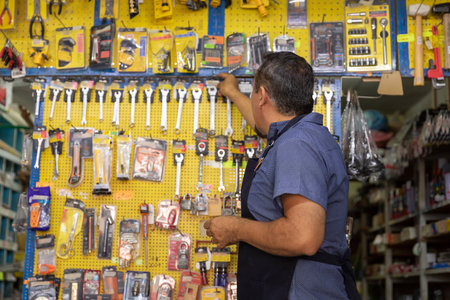 A handsome adult businessman wearing an apron, with a joyful expression, showing at camera products from his business full of hardware products.の写真素材