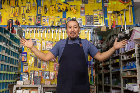 Handsome adult entrepreneur man in apron, with an expression of joy, happiness and pride in his business full of hardware products.の写真素材