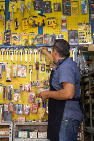A handsome adult businessman wearing an apron, with a joyful expression, showing at camera products from his business full of hardware products.の写真素材