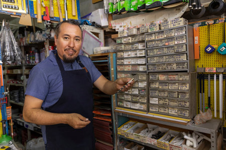 A handsome adult businessman wearing an apron, with a joyful expression, showing at camera products from his business full of hardware products.の写真素材