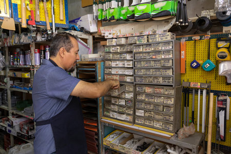 A handsome adult businessman wearing an apron, with a joyful expression, showing at camera products from his business full of hardware products.の写真素材
