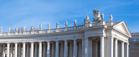 Decorative statues of religious figures carved in white marble located on the architrave surrounding St. Peter's Square in Vatican City on a sunny day with a blue skyの写真素材