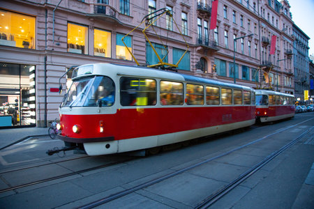 Beautiful tram running through the center of the modern and bustling city of Prague at night full of passengers and surrounded by beautiful illuminated buildings and commercial businessesの写真素材