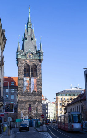 small medieval castle decorated with hanging flags and antique clock situated in the middle of the modern and busy city of Prague between 2 busy streets traveled by modern transportsの写真素材