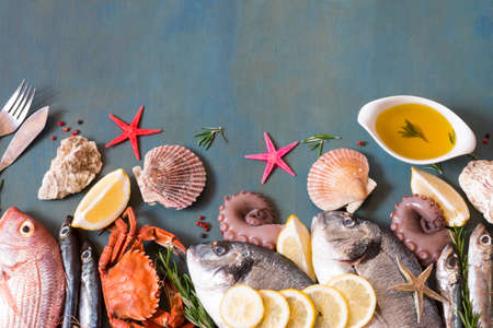 Appetizing fish and seafood on blue background with copy space, fish knife and fork.