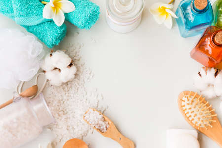 Frame of spa theme objects on a white wooden background. Bath salt, comb, lotions and towels with copy space.の写真素材