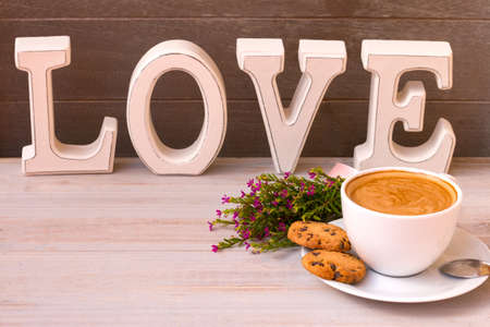 Cup of aroma coffee with coockees, flowers and word love on a light wooden background. Happy Valentine's day.の写真素材