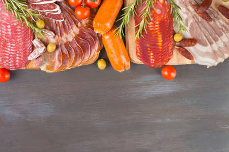 Bordure of different Spanish appetizer, like fuet, jamon, chorizo, bacon and lomo embuchado wiht spice on black wooden background.の写真素材