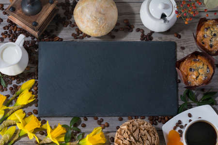 Frame of set of two muffins, cup of aroma coffee, jug of cream to coffee and daffodils on gray...