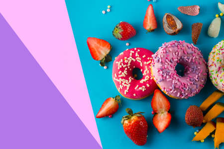 Donuts with different kinds of topping and fruits on a blue, pink and purple paper background.の写真素材
