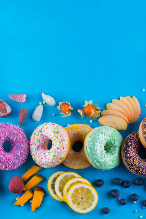 Bordure of colorful fresh donuts with different kinds of topping and fruits on a blue paper background.の写真素材