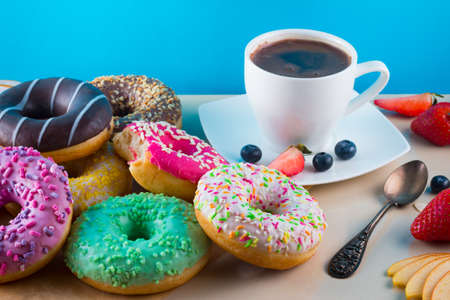 Many tasty donuts with cup of aroma coffee, fruits and one bitten pink doughnut on light stone background.の写真素材