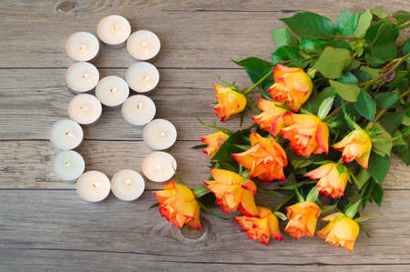 Orange rose and little burning candles in form number 8, eight on wooden background. Happy International womens day.の写真素材