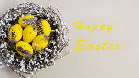 Yellow Easter eggs in the nest on light background with words Happy Easter. Traditionally holiday...
