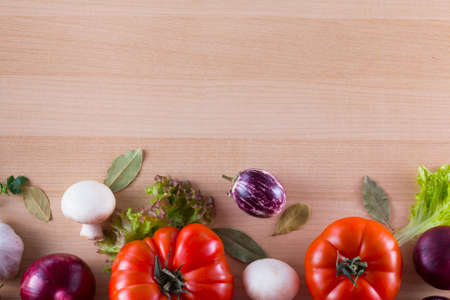 Bordure of different vegetables like tomato, eggplants, onions, salad and spices on a wooden...