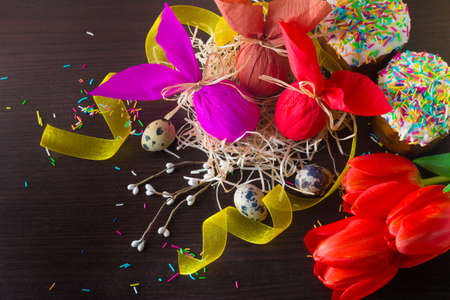 Three Easter eggs in the form of rabbit in the nest with willow branch, red tulips and russian easter cakes.の写真素材