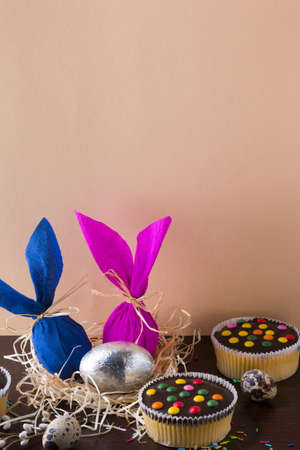Easter eggs in the form of rabbit on light brown background with cupcakes.