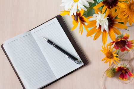 Bouquet of summer flowers like heliopsis, chamomile, rudbeckia and gaillardia with notebook and pen. Top view.の写真素材