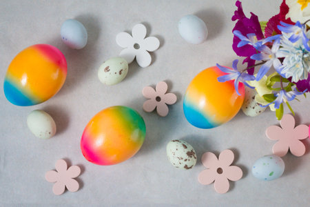 Easter colored rainbow eggs with spring flowers, top view on light gray backgroundの写真素材