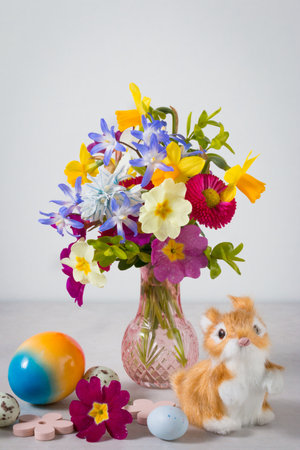 Cute Easter bunny and colorful rainbow Easter eggs with spring flowers on light gray stone background.の写真素材