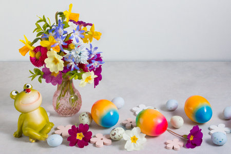 Colorful rainbow Easter eggs and funy frog with spring flowers on light gray stone background.の写真素材