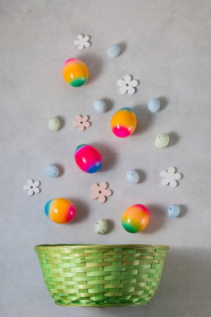 Rainbow Easter eggs with spring flowers falling down into a wicker basket on light gray background. easter decoration.の写真素材