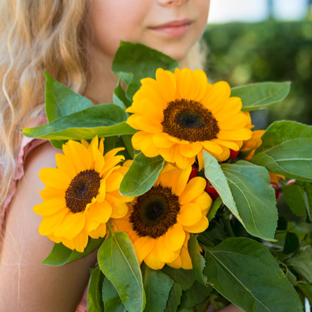 Girl holds sunflower. Pretty young girl holds a yellow sunflowers in the green background.の写真素材