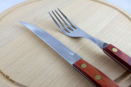 Fork and knife with red wooden handle on a plate of natural wood の写真素材