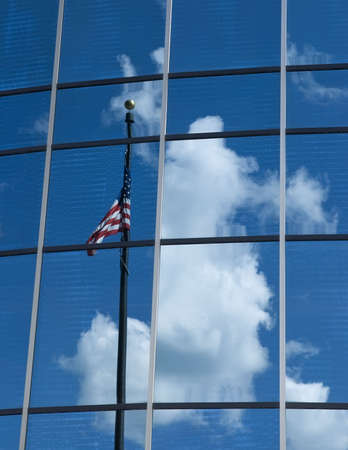 Flagmire - the observed reflection in a glass building of an American Flag twisted around its own flagpole in an attempt to display its colors, venetian blinds visible inside the buildingの写真素材
