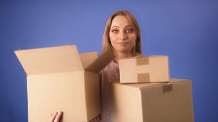 Young caucasian woman with packed cardboard boxes and surprised face isolated on the blue...