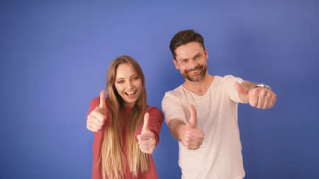 young happy couple with thumbs up isolated on the blue background. Copy space.