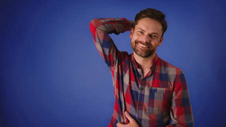 Attractive happy bearder caucasian man posing with hand on his head over the blue background. High...
