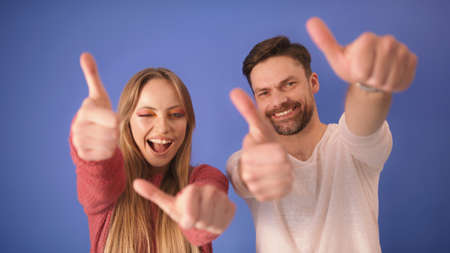 young happy couple with thumbs up isolated on the blue background. High quality photoの写真素材