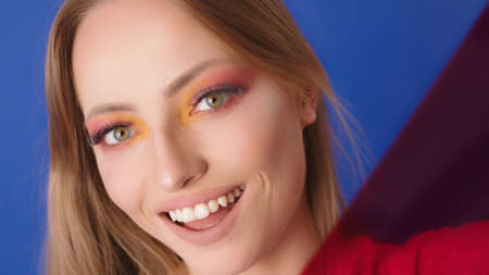 Beauty portrait shot. Young caucasian woman with big smile, make up and red film gel in front of her face. Diagonal, copy space.の写真素材
