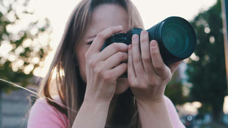 Outdoors photoshoot. Female photographer looking through the viewfinder of her dslr camera. High quality photoの写真素材