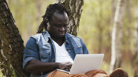 New normal. Remote work concept. African man using laptop in the nature. High quality photoの写真素材