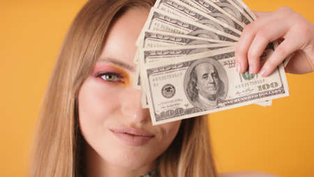 Portrait shot of woman with makeup covering half of the face with dollars. High quality photo