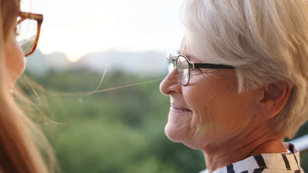Close up shot of senior mother and adult daughter looking in at each other on the balcony. High...