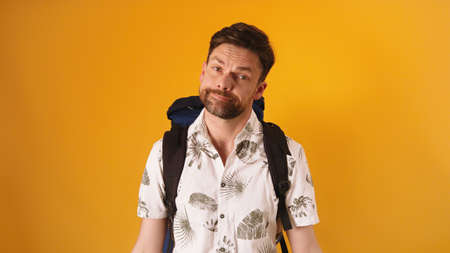 Disappointed face expression on young bearded traveler with backpack isolated on orange background....