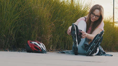 Young attractive woman adjusting rollerskates while sitting in the park. . High quality photo