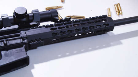 Tactical rifle with a colimator sight and some ammunition on the table.