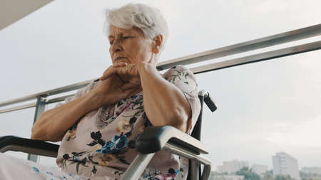 Pensive sick disabled old lady sit in wheelchair look in distance feel lonely at home or retirement house. High quality photoの写真素材