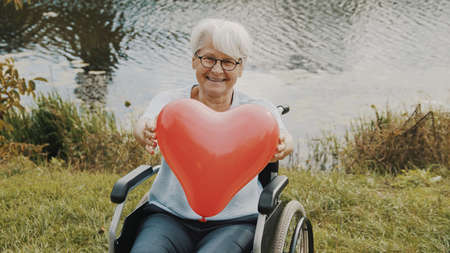 Senior woman holding heart shaped balloon near the river. Love and care concept. High quality photoの写真素材