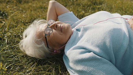 senior retired woman with headphones lying on the grass and listening to the music. High quality photoの写真素材