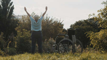 Senior woman with outstretched hands in the nature in front of the wheelchair. High quality photo