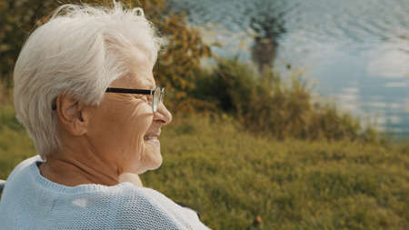 Close up, senior gray haired woman in the wheelchair enjoying autumn breeze near the river. High quality photoの写真素材