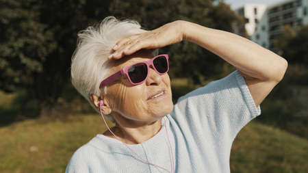 Senior woman with pink sunglasses in the park looking at the distance. High quality photoの写真素材